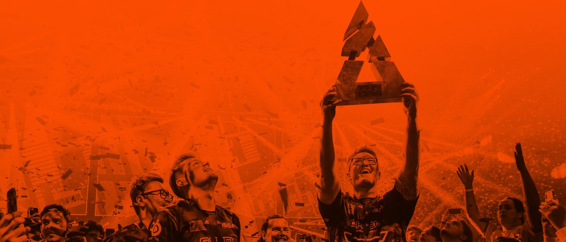 An esports player celebrates a win with a trophy above their head and confetti falling.