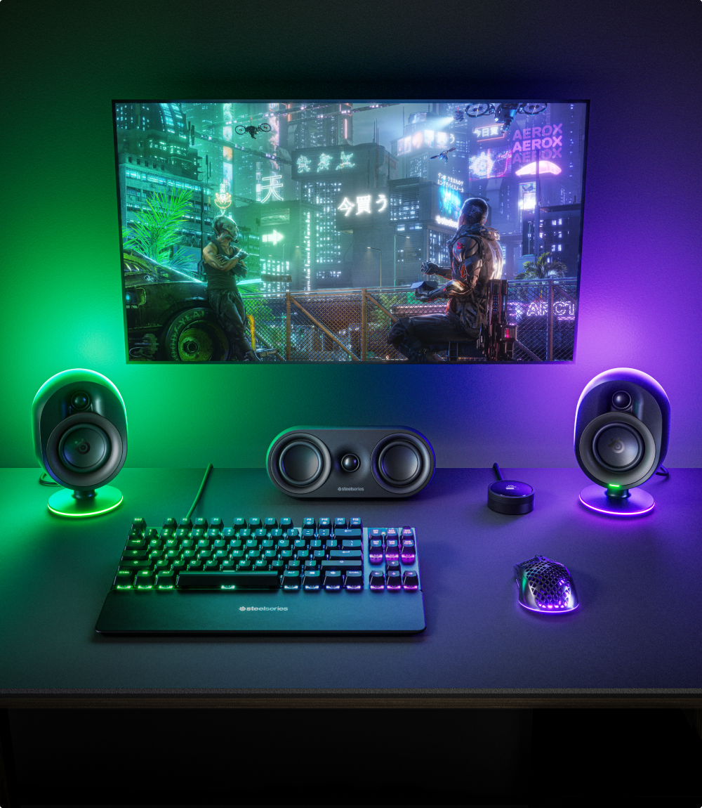 A desktop setup with Arena 9 speakers glowing with green and purple RGB.